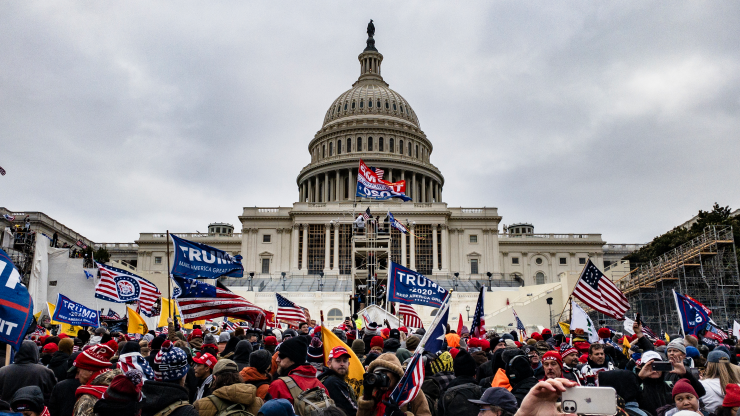 Insurrectionists stand waving flags in front of the Capitol Building in Washington, D.C. on January 6. There are multiple "Trump 2020" and American flags.