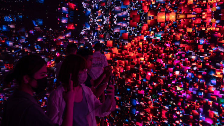 Visitors stand in a room wearing face masks surrounded by square boxes of red and blue images in a metaverse exhibit in Hong Kong.