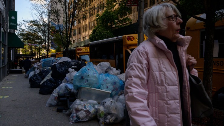 Pedestrians pass by trash bags piled on a street in Manhattan .
