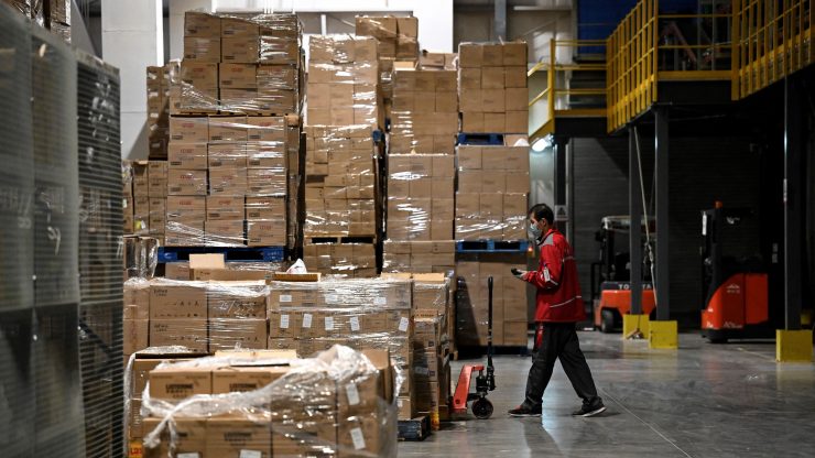 A worker in front of a large pile of boxes in a warehouse.