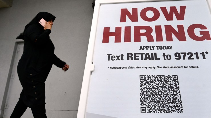 A woman wearing a face mask walks past a "Now Hiring" sign in front of a store on January 13, 2022 in Arlington, Virginia.