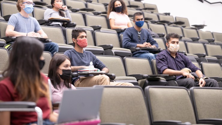 Masked students sit spaced out in a lecture hall.