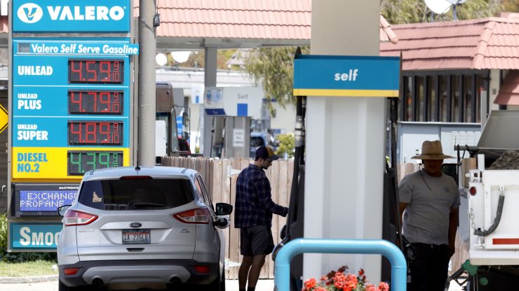 People pumping gas at a Valero gas station, with gas prices posted in the background.