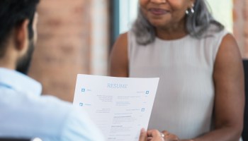 A man holds the resume of a woman of color during a job interview.