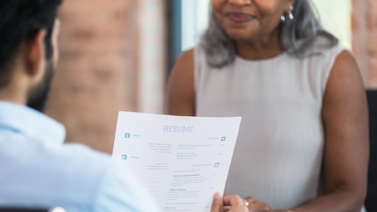 A man holds the resume of a woman of color during a job interview.
