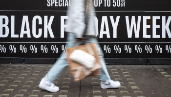 A shopper with a handbag walks past a sign referring to Black Friday.