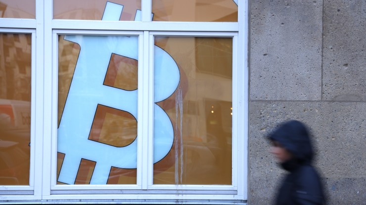 A young woman walks past a Bitcoin symbol in the window of a company that offers blockchain application services .