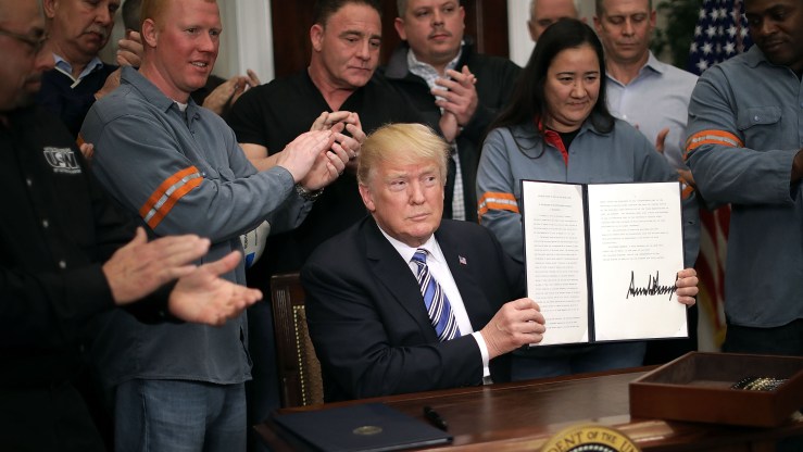Surrounded by applauding steel and aluminum workers, U.S. President Donald Trump holds up the Section 232 Proclamation on steel imports that he signed in the Roosevelt Room in the White House on March 8, 2018.