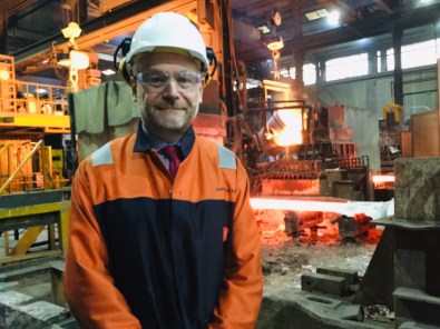 James Brand of United Cast Bars wears protective goggle and a helmet in front a foundry.