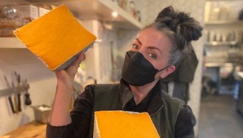 Lydia Clarke, owner of DTLA Cheese, wears a face mask and holds two wedges of cheese.