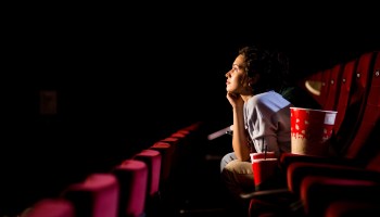 A woman views an event in an otherwise empty theater with her popcorn and drinks by her side.