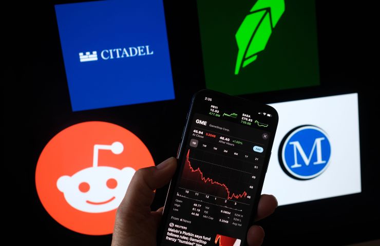 A person checks GameStop stock on a smartphone with the Reddit, Citadel, Robinhood and Melvin Capital logos in the background.
