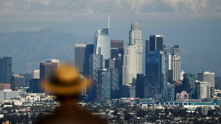 A person looks toward snow-topped mountains behind the Los Angeles downtown skyline following heavy rains.