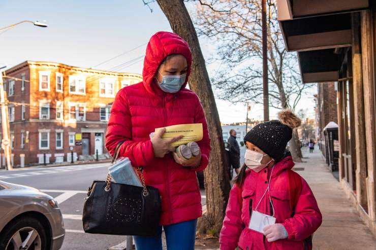 A parent and child walk down the street with rapid at-home COVID tests.