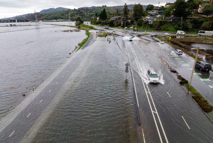 An aerial picture taken on January 3, 2022, shows vehicles driving along a road flooded with ocean water during the "King Tide" in Mill Valley, California.