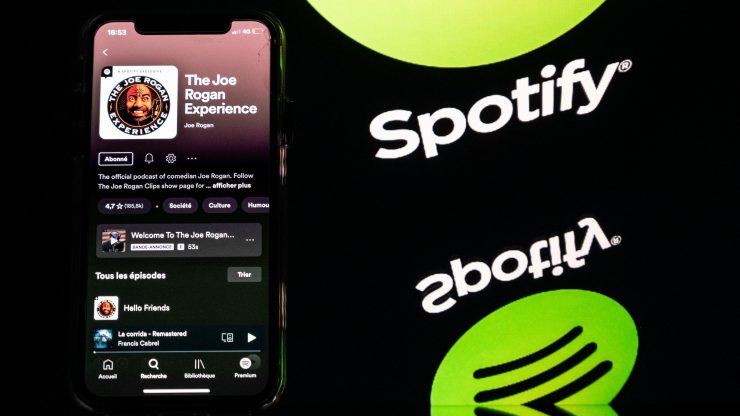 Image of spotify logo next to a phone displaying the "Joe Rogan Experience" podcast
