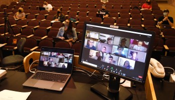Remote students appear on computer screens in a college lecture hall.