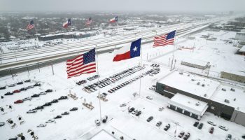 The Texas and American flags over a snow-blanketed parking lot in Texas.