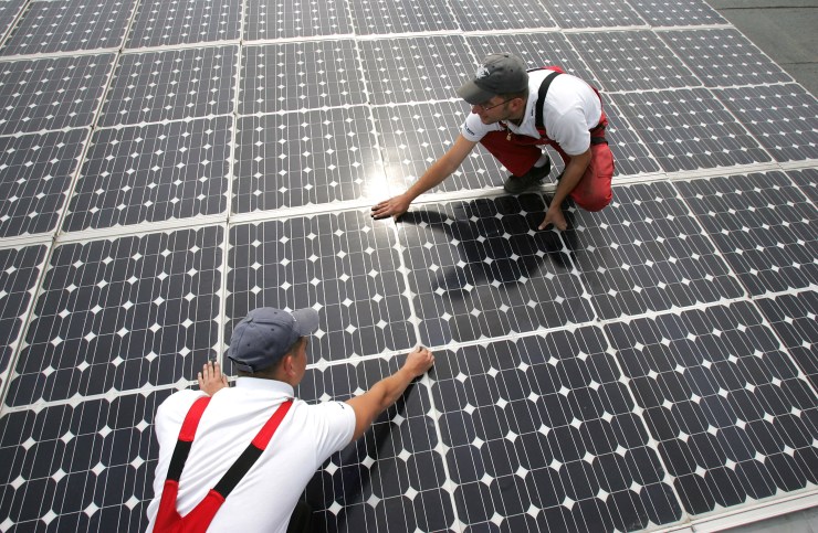 Two workers maintain solar panels on the roof of a warehouse in Buerstadt, Germany.