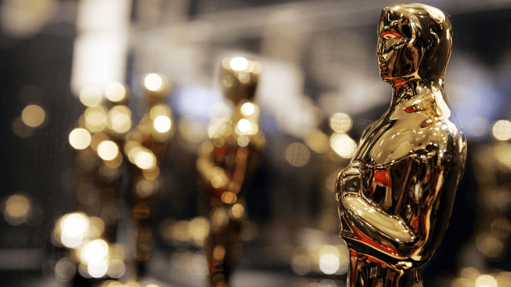 A closeup image of the golden Oscar statue is featured on the right side of the image, with blurred Oscars statuettes in the background.