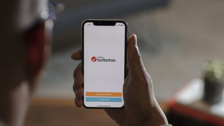 A person holds their smart phone which includes the title "Intuit turbotax."