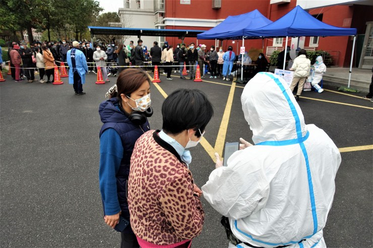 A worker in hazmat suit helps residents to book a PCR test through a mobile app during a mandatory PCR testing in a Shanghai community in March 2022 (Charles Zhang/Marketplace)