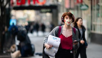 Woman walking on a busy street with a mask on.