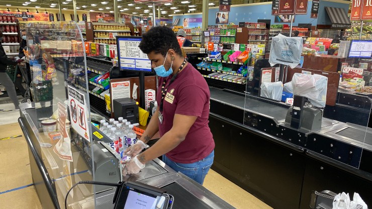 A checkout clerk works behind a plexiglass divider at the ShopRite Supermarket amid the coronavirus pandemic on April 24, 2020.