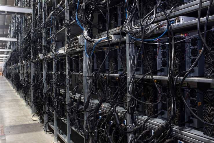In a warehouse, rows of bitcoin machine can be seen stored in cubicles with wires sticking out.