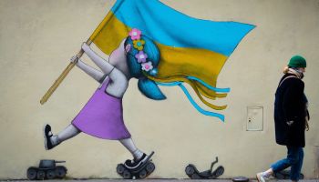 A bystander walks past a fresco by street artist Seth depicting a girl with a Ukrainian flag walking on tanks in Paris on March 01, 2022.