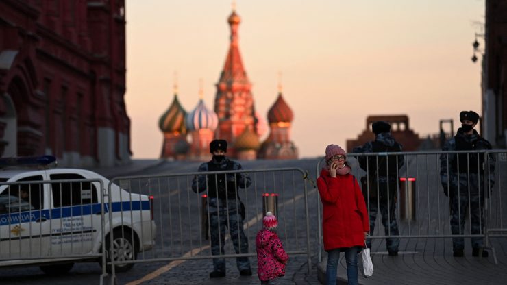Image of woman on the phone and child standing in front of Red Square in Moscow with police behind them.