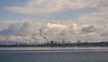 An oil refinery with smoke billowing under cloudy skies.