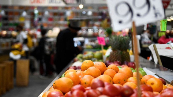 Oranges, accompanied by a blurred out sign listing their price, are displayed at a produce stall.