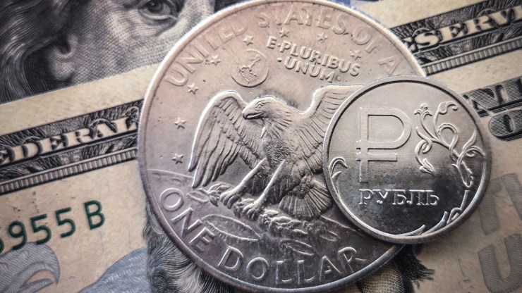A Russian ruble coin is pictured with US dollar bills and a one dollar coin in Moscow, on March 15, 2022.