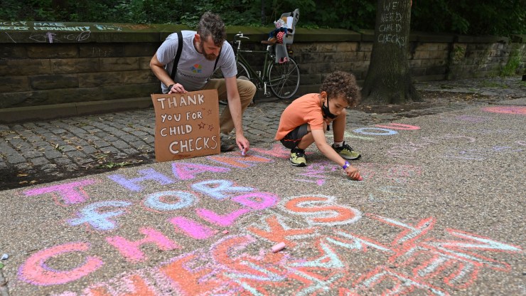 Justin Ruben and Rime Leonard draw with chalke to celebrate new monthly Child Tax Credit payments and urge congress to make them permanent outside Senator Schumer's home on July 12, 2021 in Brooklyn, New York.