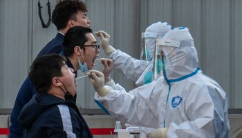 Health workers dressed in protective clothing give nucleic acid tests to men at a mass testing site to prevent COVID-19 on March 14, 2022 in Beijing, China.