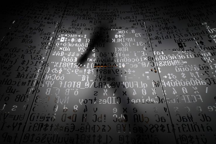 A shadow of a person walking behind a glass wall with machine coding symbols.