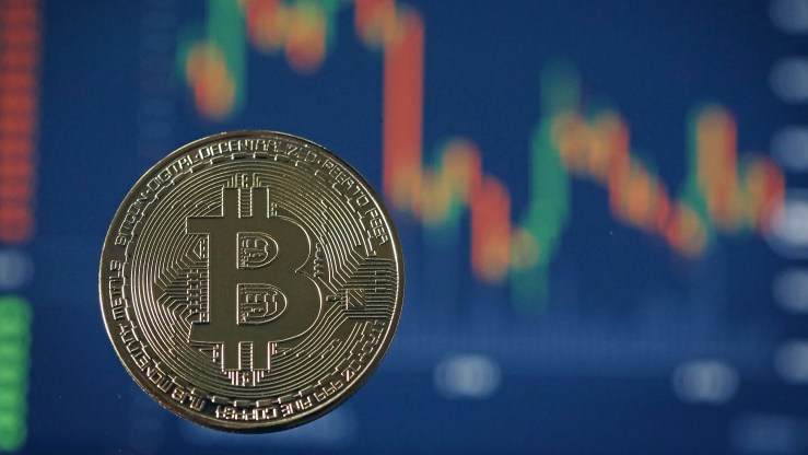 A visual of a bitcoin is seen in front of a stock market graph.