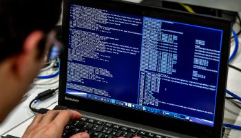 A man types on a Lenovo laptop, in a coding language.