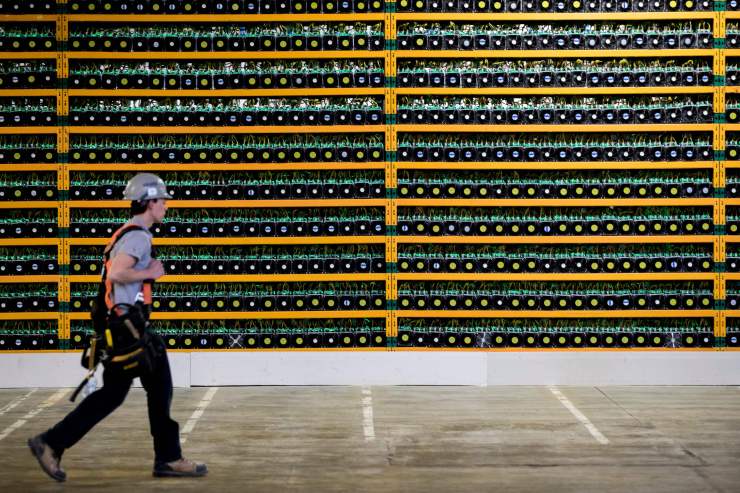A construction worker walks past several bitcoin mining rigs.