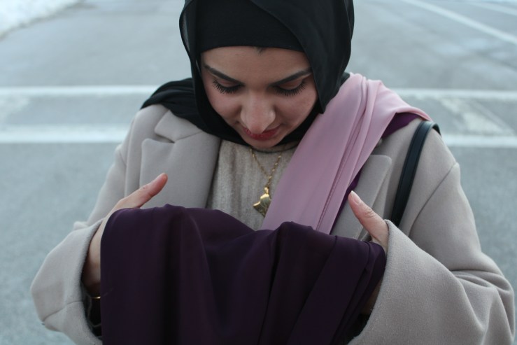 Israa Enan examines a maroon hijab, holding it in her hands.