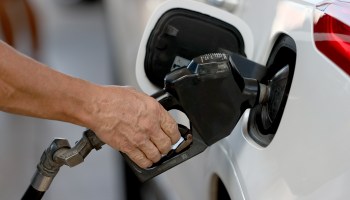 Close-up of a person's hand putting a gas pump into a car's tank.