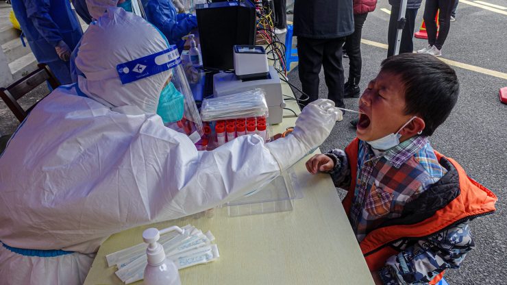 A person in white protective clothing swabs the mouth of a child being tested for COVID-19 in Shanghai.