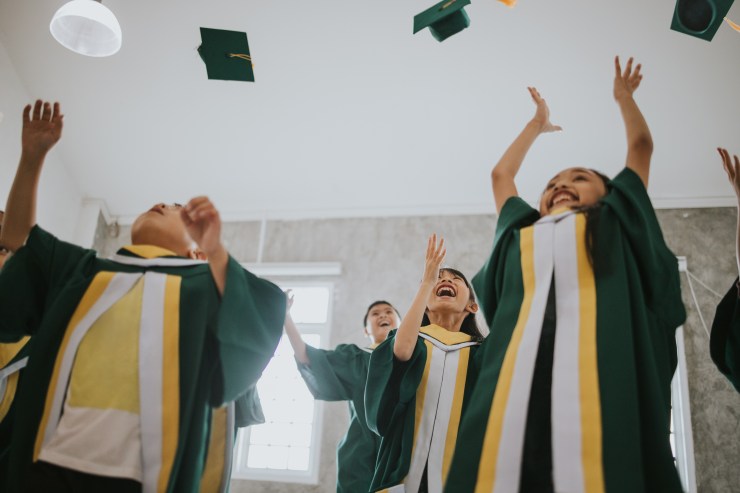 A group of children in graduation robes throws their hats in the air.