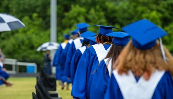 Former students of Jefferson County Public Schools, dressed in cap and gown, line up to approach the stage during a makeup graduation ceremony.