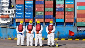 Employees wearing personal protective equipment (PPE) look on by a cargo ship at a port in Qingdao in China's eastern Shandong province on January 14, 2022.