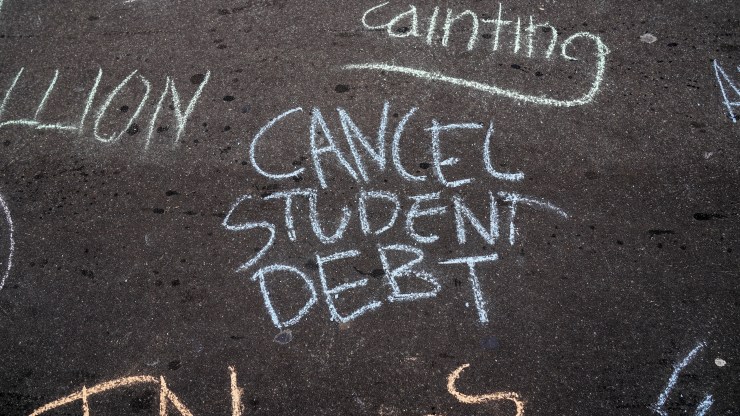 "Cancel Student Debt" is written on concrete with chalk.