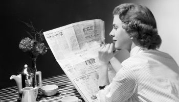 A woman reads a newspaper in the1950s.