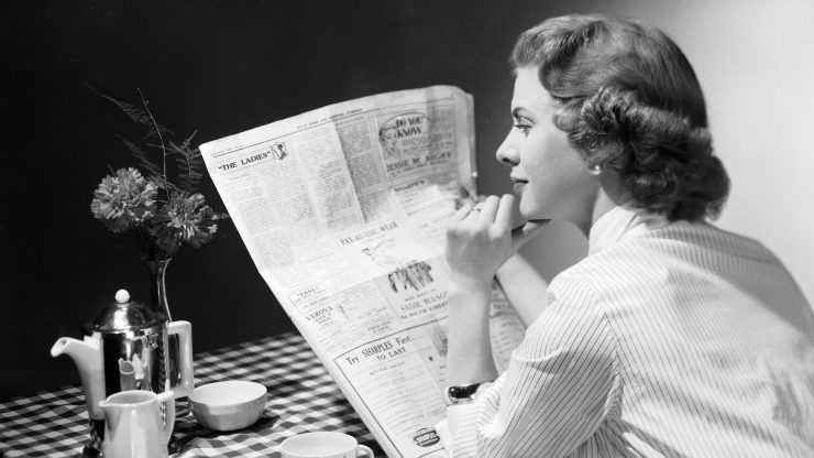A woman reads a newspaper in the1950s.