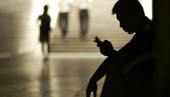 In silhouette, a man looks at his mobile phone.